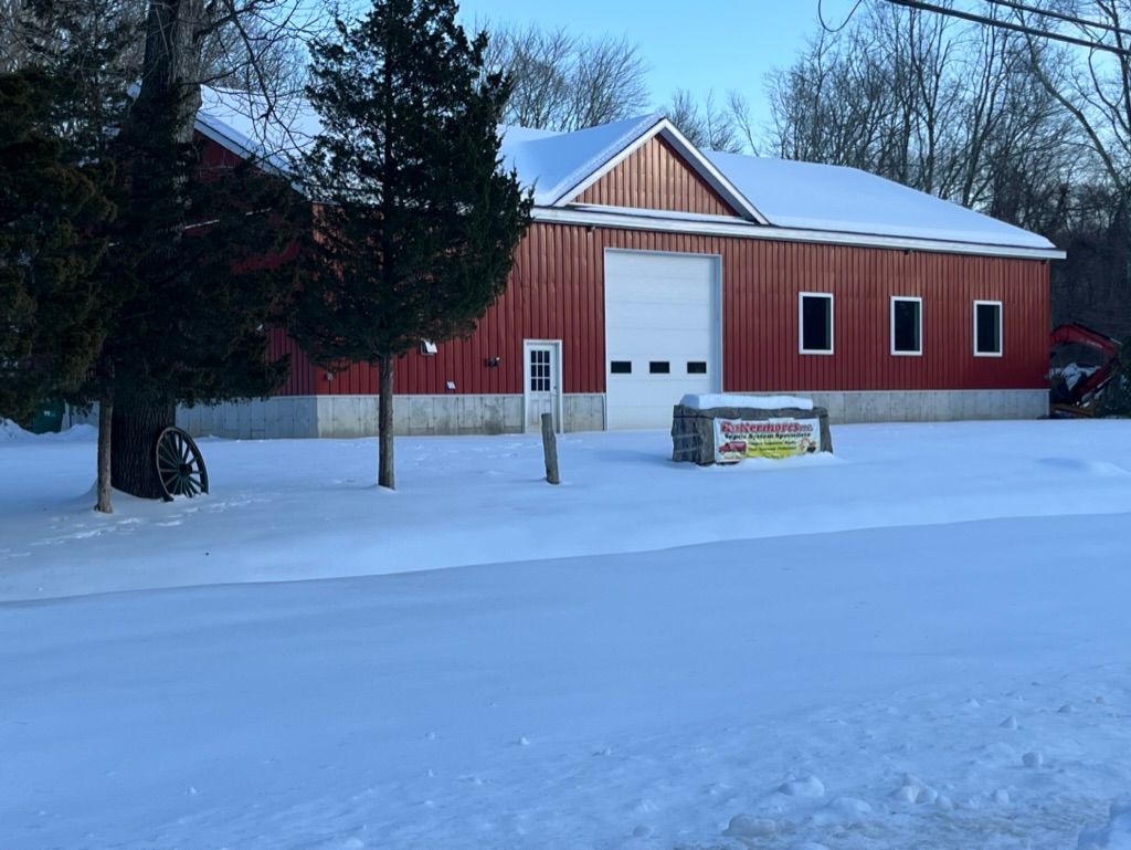 Red barn with a white garage door, small windows, and snow-covered surroundings.