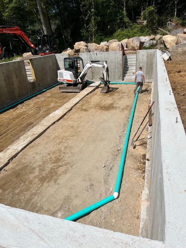 Construction site: Concrete walls with an excavator, worker, and green pipes.