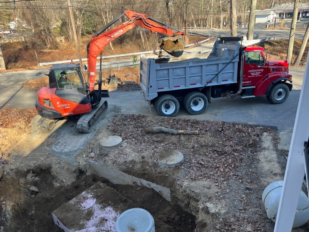 Excavator loading dirt into a red dump truck at a construction site.