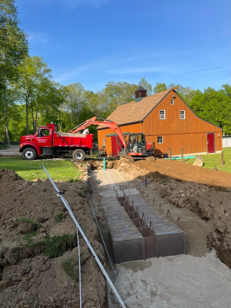 Construction site: Red truck, excavator, barn, trench, and gravel.