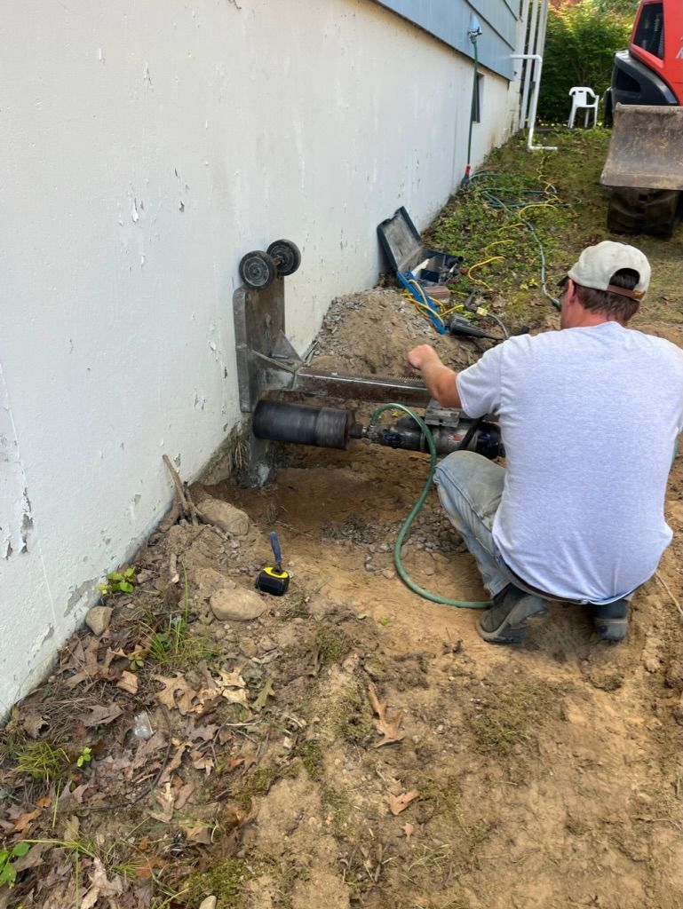 Person kneeling outside a building, working on pipes. A backhoe is nearby.