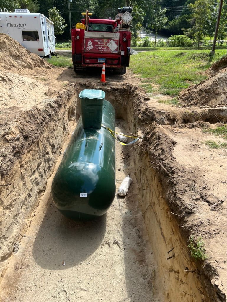 Green propane tank in a trench with a red truck in the background, outdoors.
