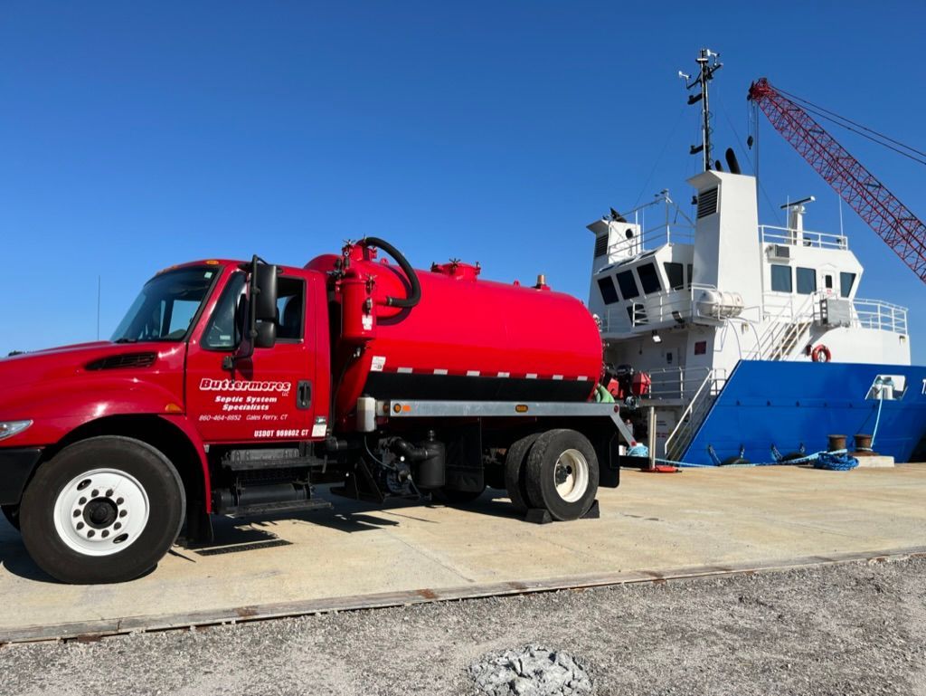 Red tanker truck parked next to a blue and white ship at a dock on a sunny day.