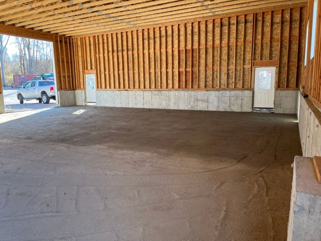 Open-air carport with a gravel floor, wooden supports, and two doors. A white truck is visible outside.