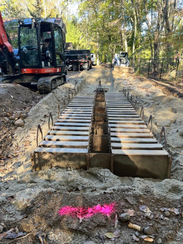 Construction site: excavator, concrete forms in a trench, pink spray paint marking.