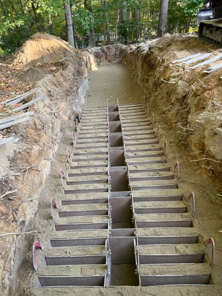 Trench with stair steps under construction, surrounded by dirt and trees.