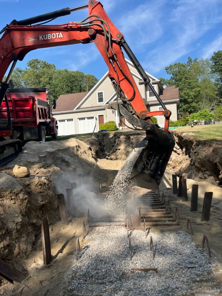 Red excavator dumping gravel into a trench in front of a house.