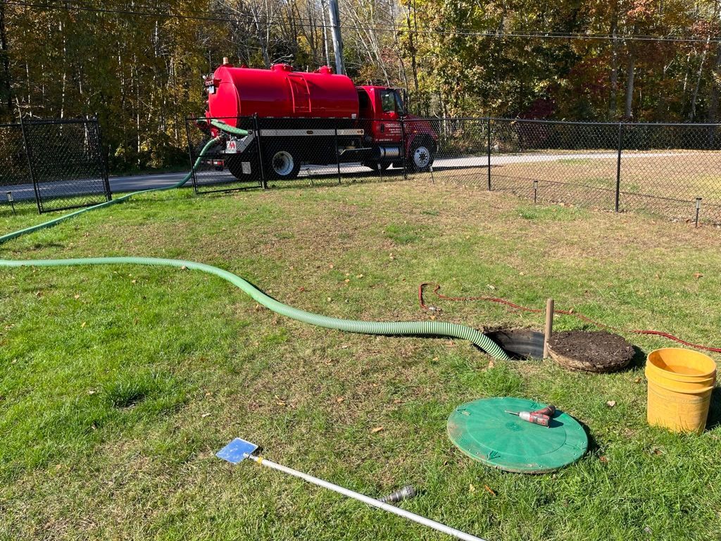 Red septic tank truck pumping from a septic system in a grassy area.