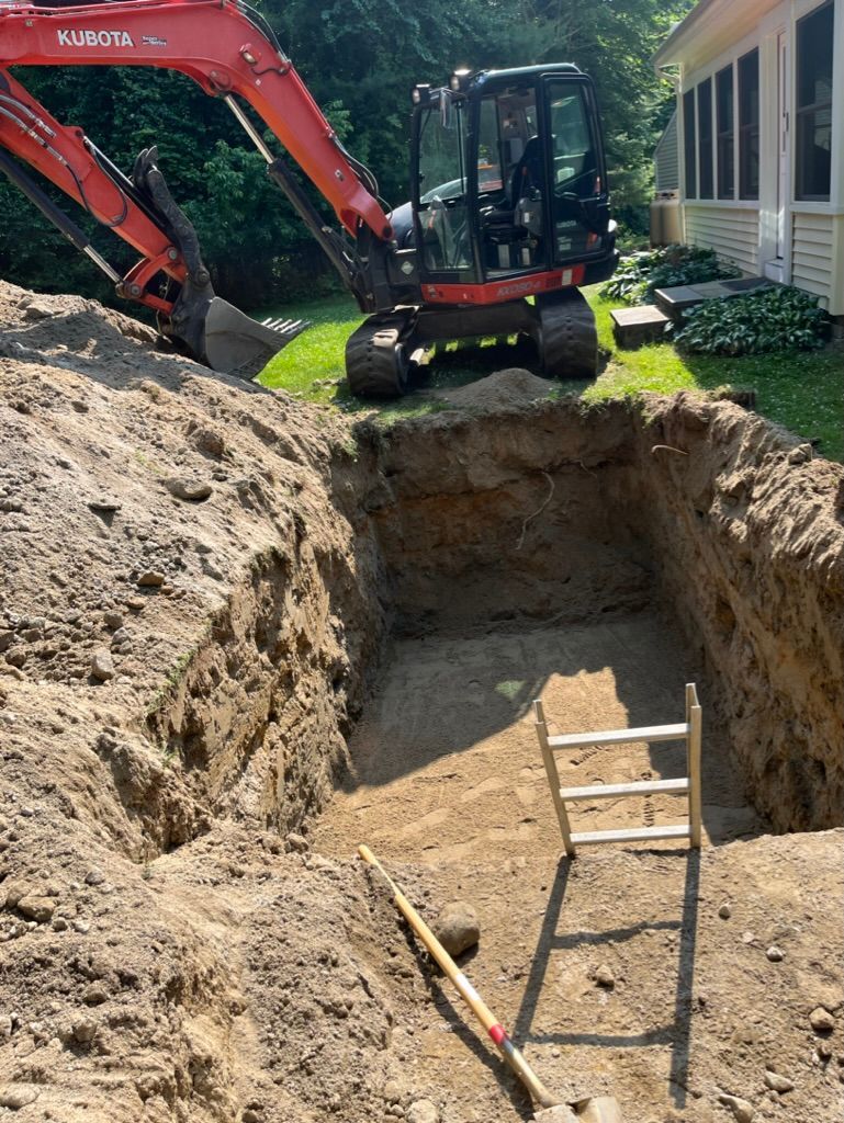 Red excavator digging a rectangular pit in a sunny outdoor setting with a ladder inside the pit.
