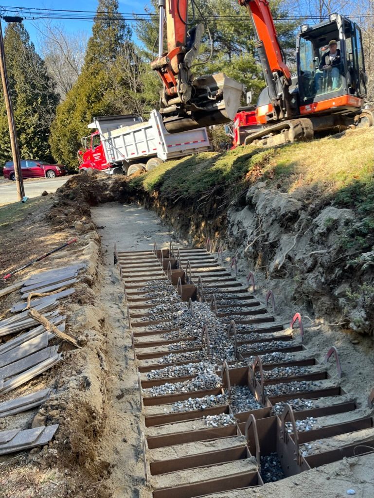 Construction site with an excavator and dump truck. Trench with installed wood forms for steps.