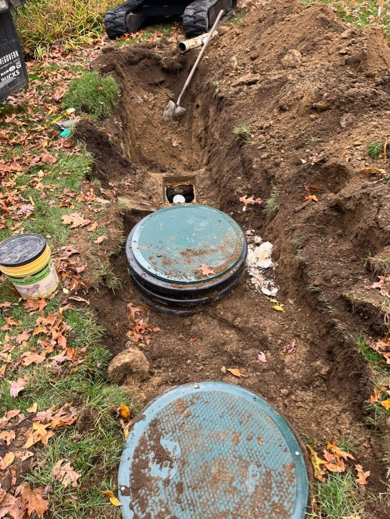 Septic tank lids in an open trench, surrounded by dirt and grass; construction site.