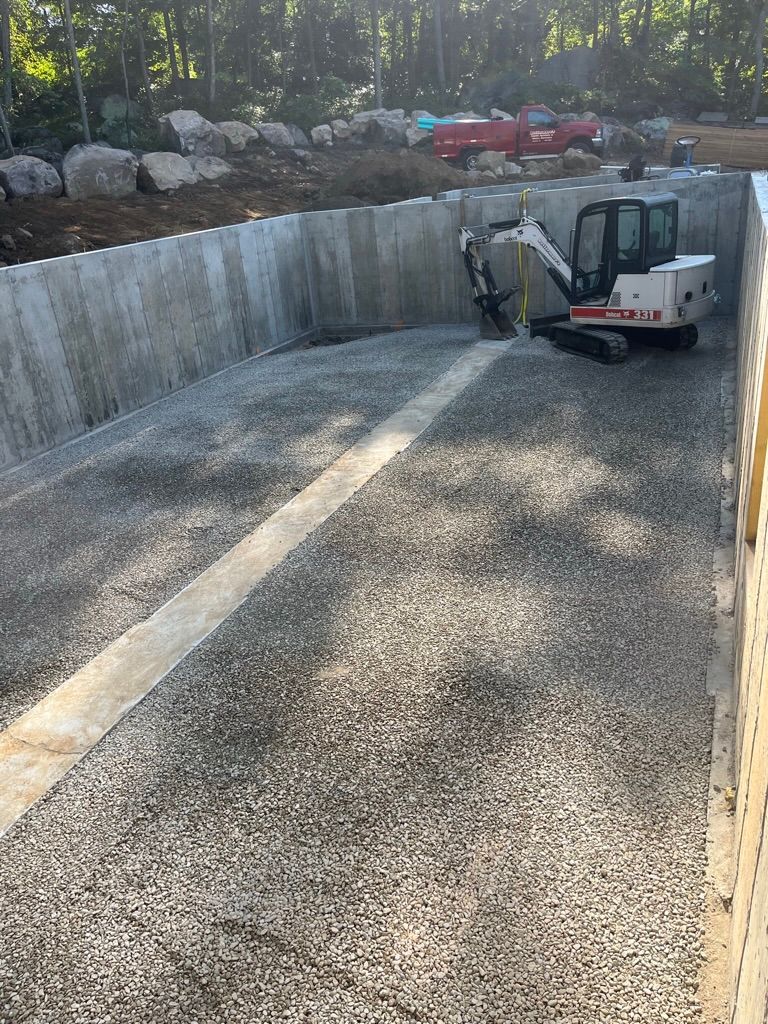 A small excavator works inside a concrete structure filled with gravel.
