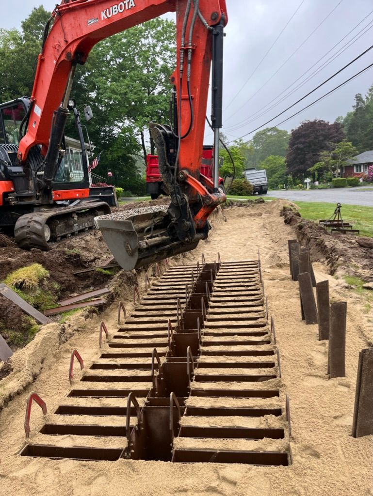 Orange excavator digging in a sandy trench; metal structures visible.
