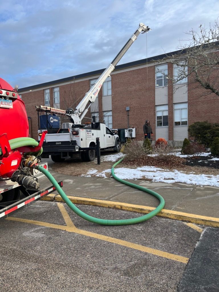 Truck with extended boom servicing a building. Hose connected to a red tank. Snow and cloudy sky.