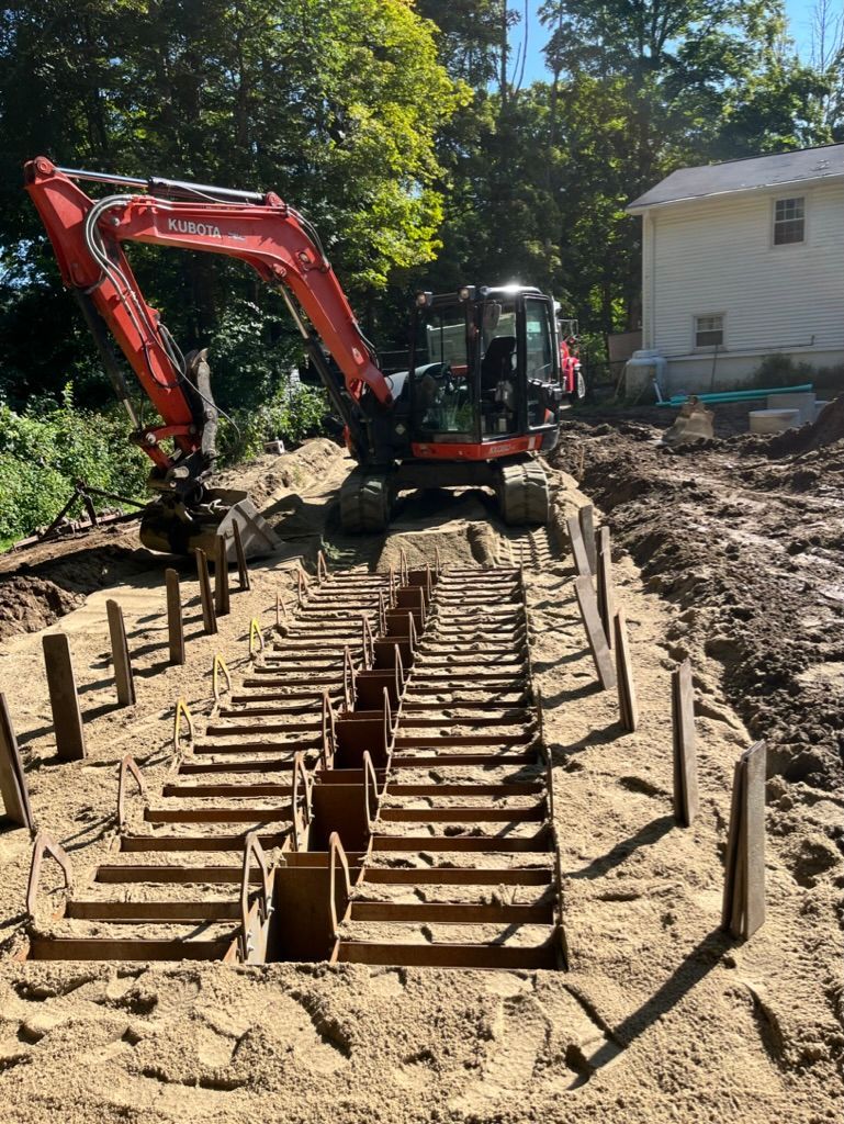 Red excavator at a construction site, digging a trench with wooden supports.