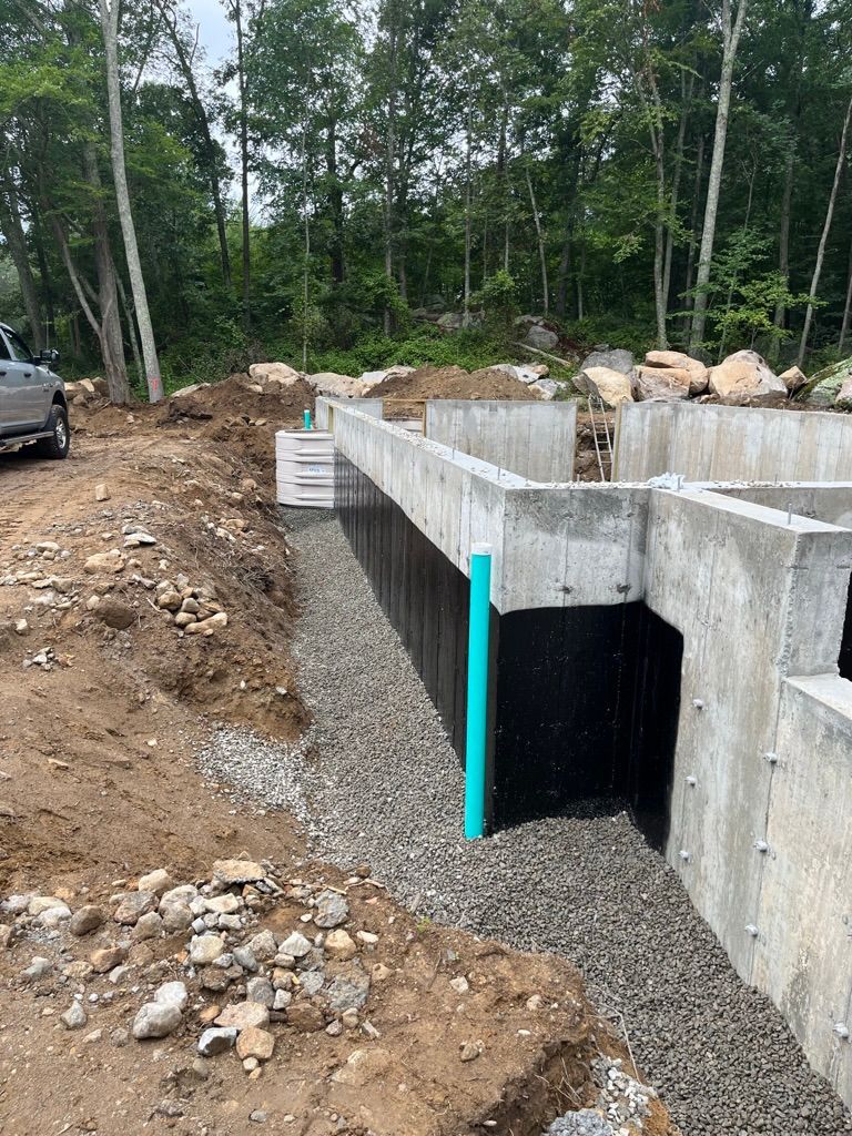 Foundation construction with a gravel drainage system against a black waterproof membrane.