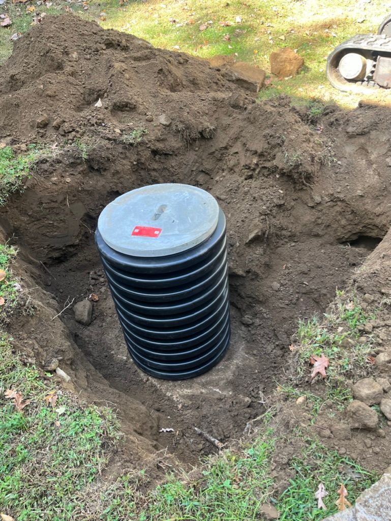 Black corrugated well in a dirt excavation with a gray lid.
