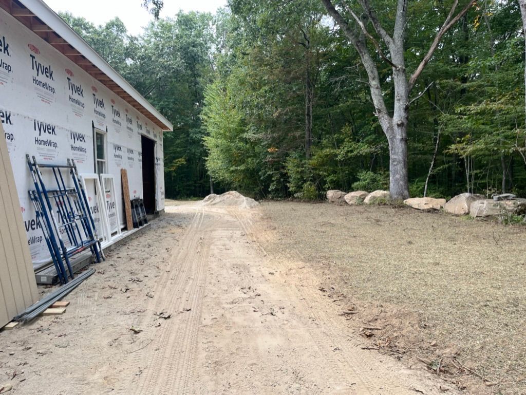 Construction site: garage with blue scaffolding, unpaved driveway, trees in background.