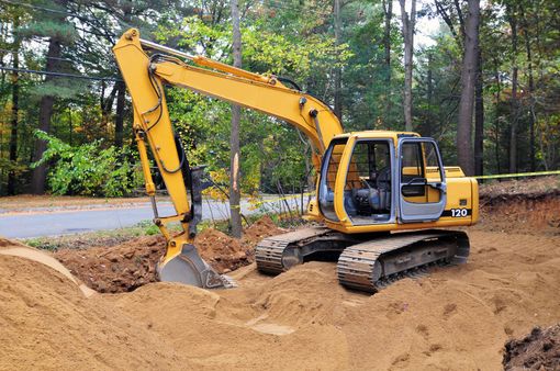 Yellow excavator digging in a dirt pit near a road and trees.
