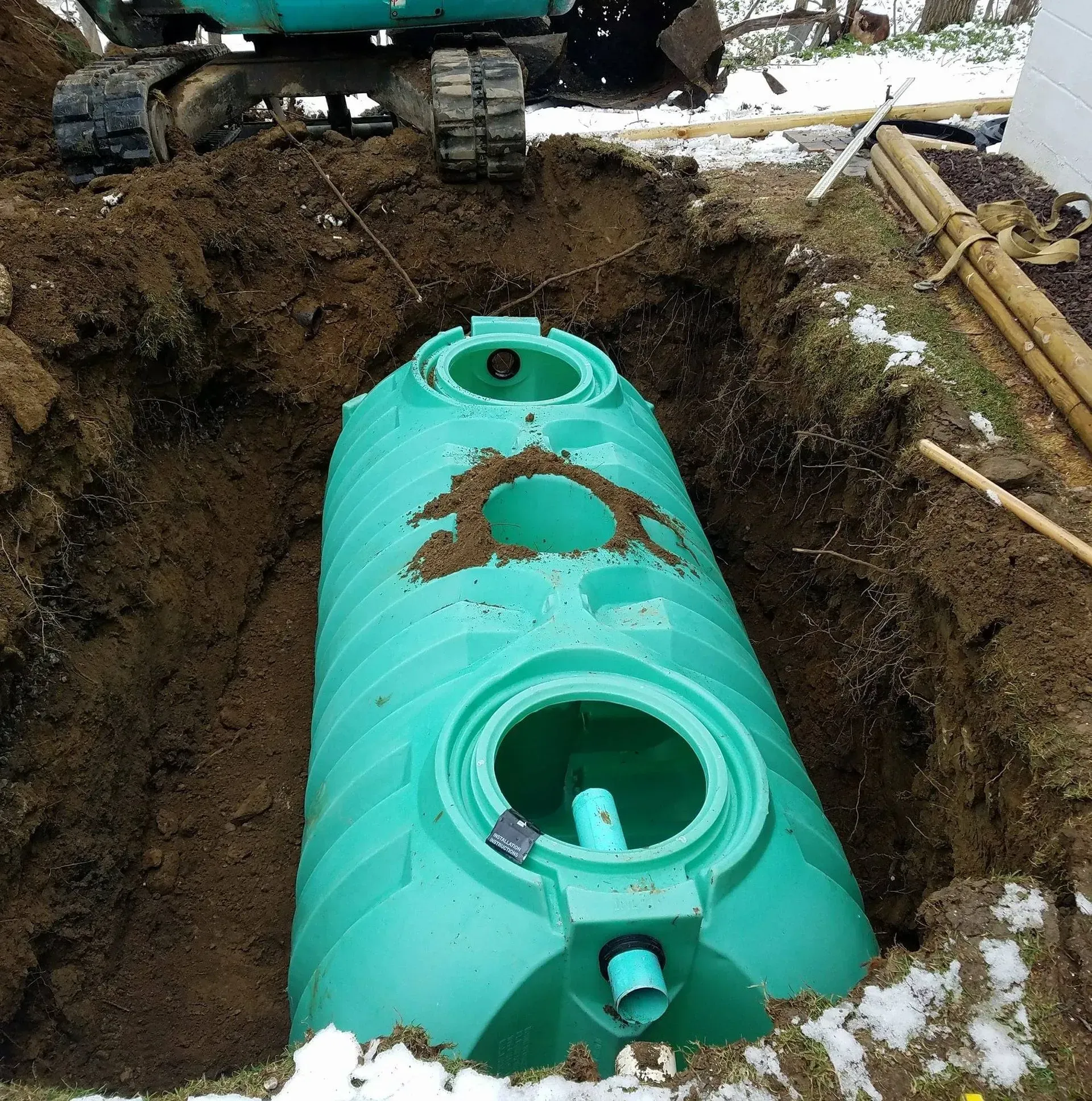 Green septic tank in a trench, partially buried, with a small excavator visible.