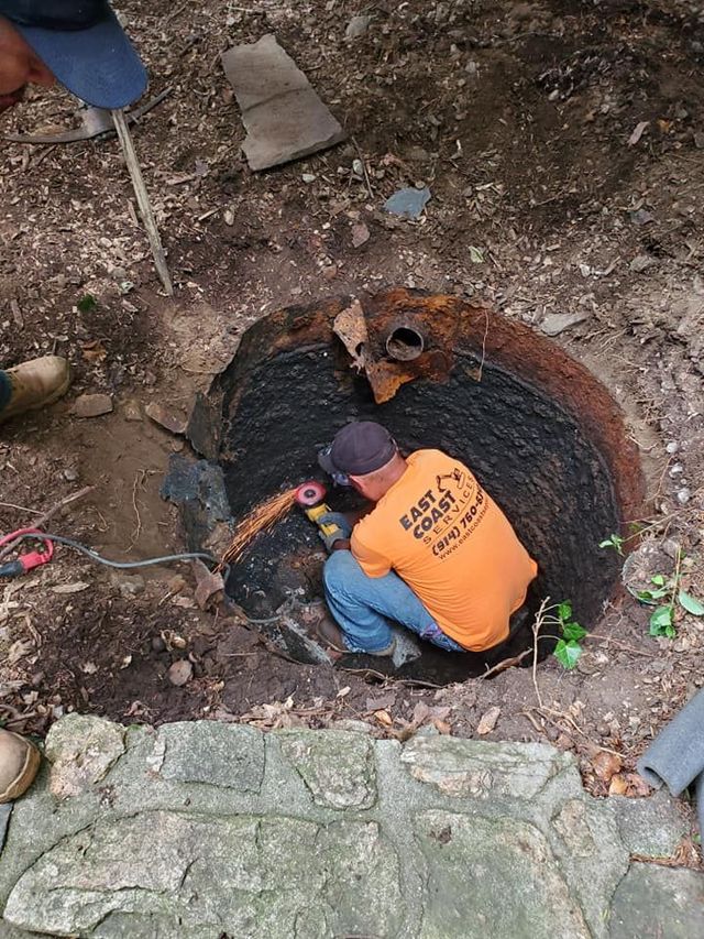 Man cutting into a rusted, circular object in the ground, possibly a tank or manhole.
