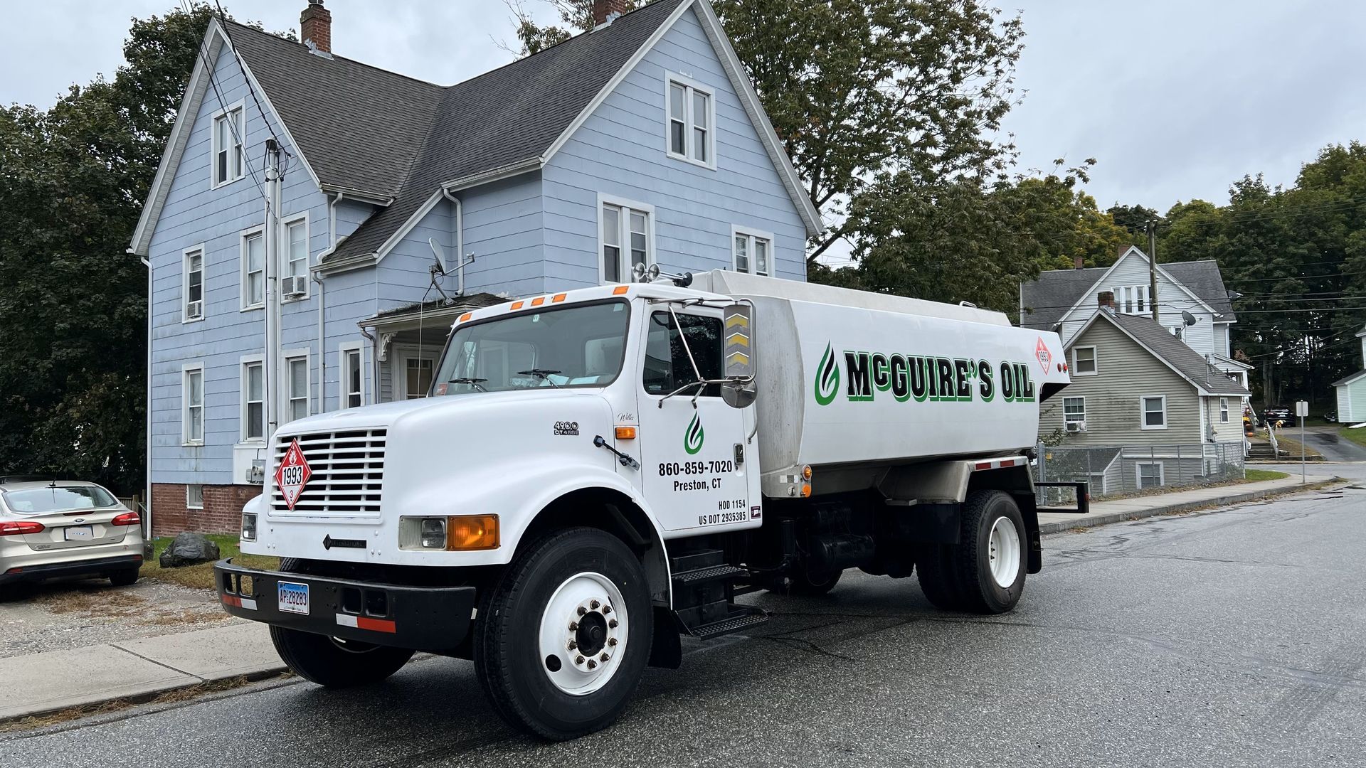 White oil truck parked on a street beside a blue house