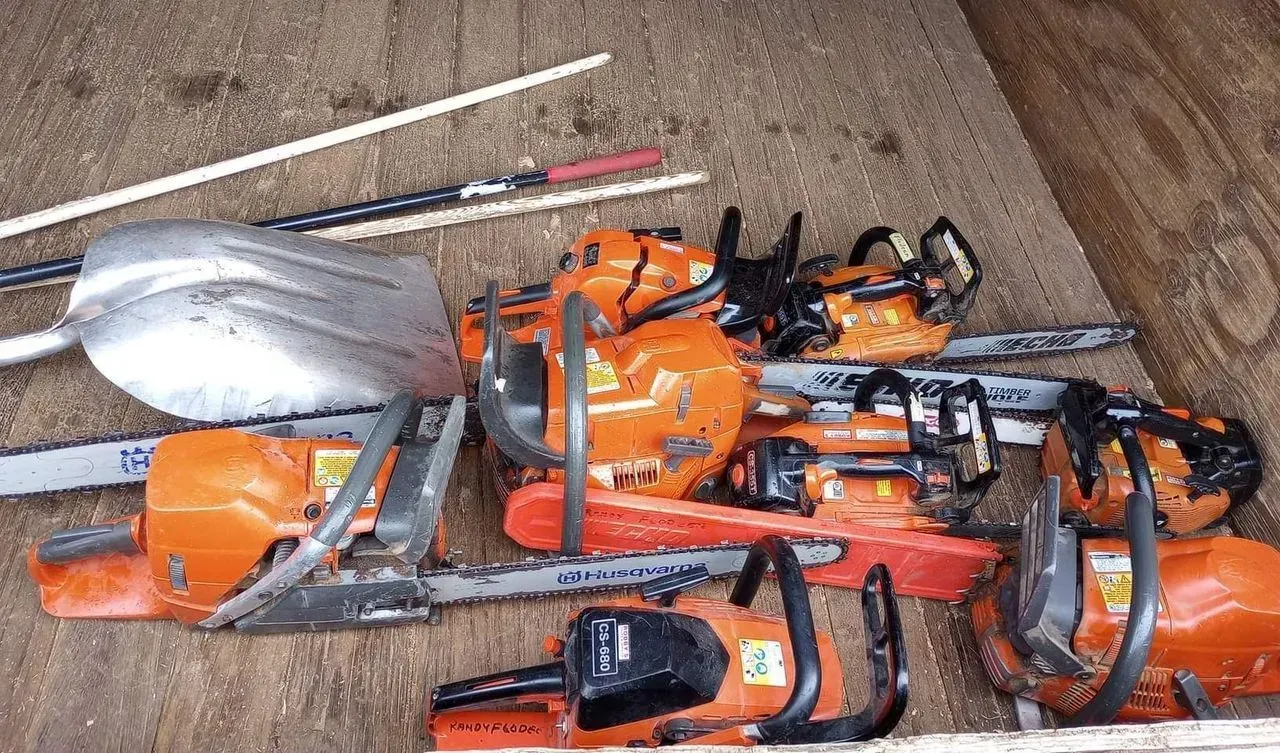 Pile of orange chainsaws and a silver shovel on wooden surface.