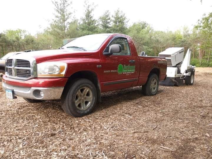 Red Dodge truck with tree stump grinder attached, parked on wood chips.