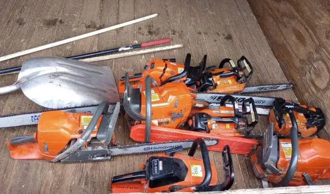 Pile of orange chainsaws and a silver shovel on a wooden surface.