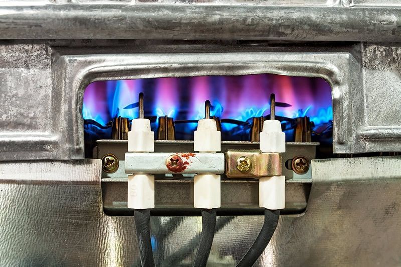 Gas stove burner with blue flames beneath metal grate and connectors
