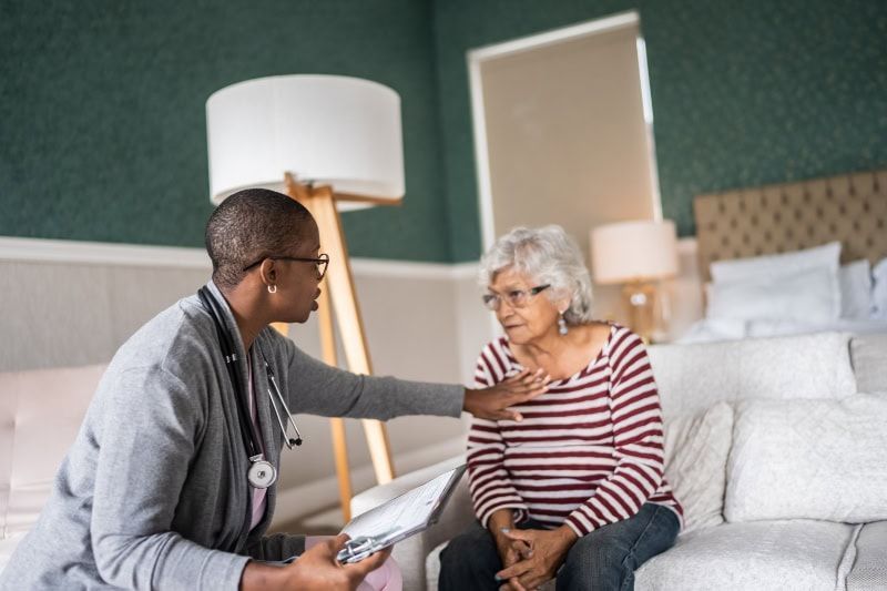 Doctor speaking with an elderly patient in a bright bedroom, holding her hand during a visit