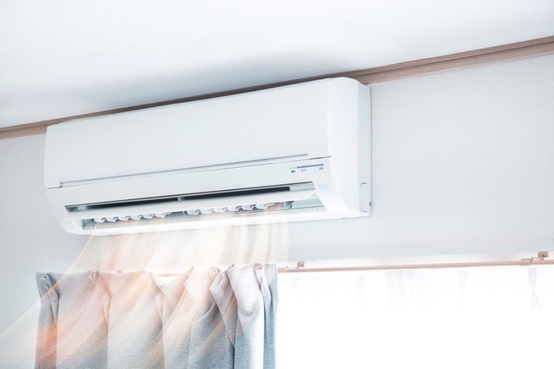 White wall-mounted air conditioner above a window with light curtains