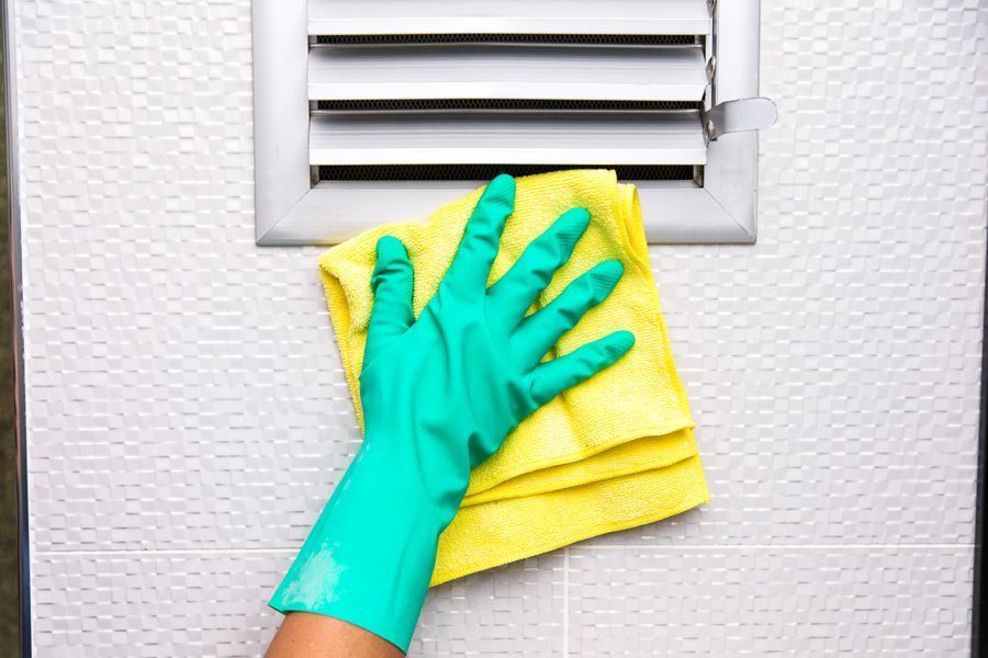 Gloved hand wiping a wall vent with a yellow cloth