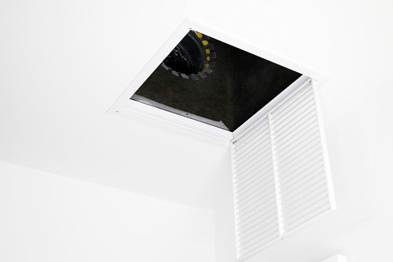 Open ceiling hatch with a dark attic space visible above white walls and shutters