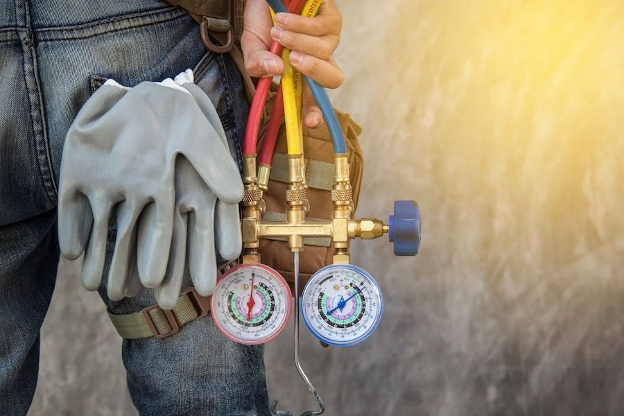 Gloved worker holding HVAC manifold gauges with colored hoses against a bright background