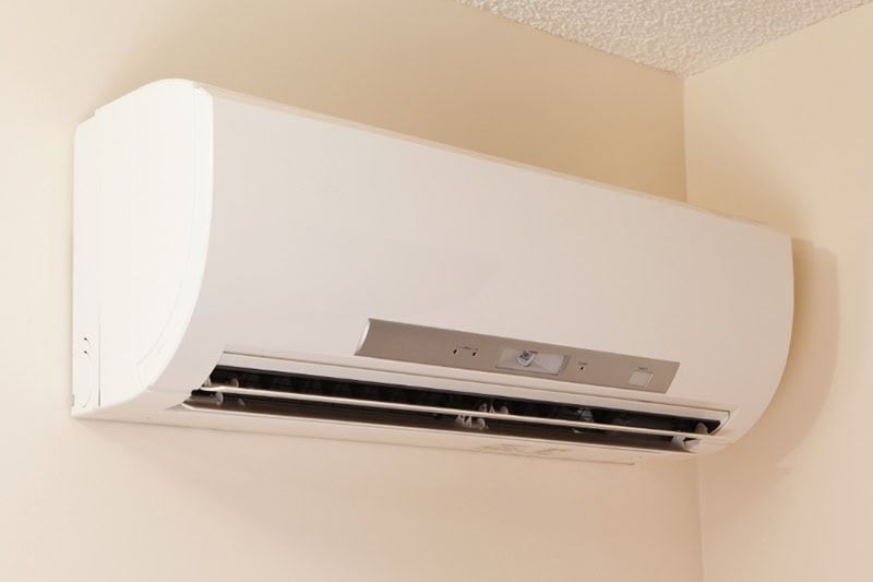 White wall-mounted air conditioner on a beige wall, with the vent open and control panel visible