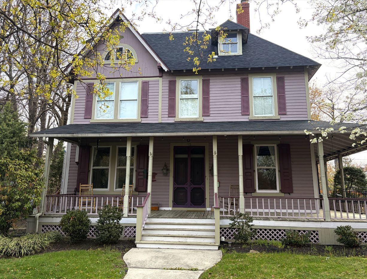 Two-story purple house with porch, white trim, and front steps under trees