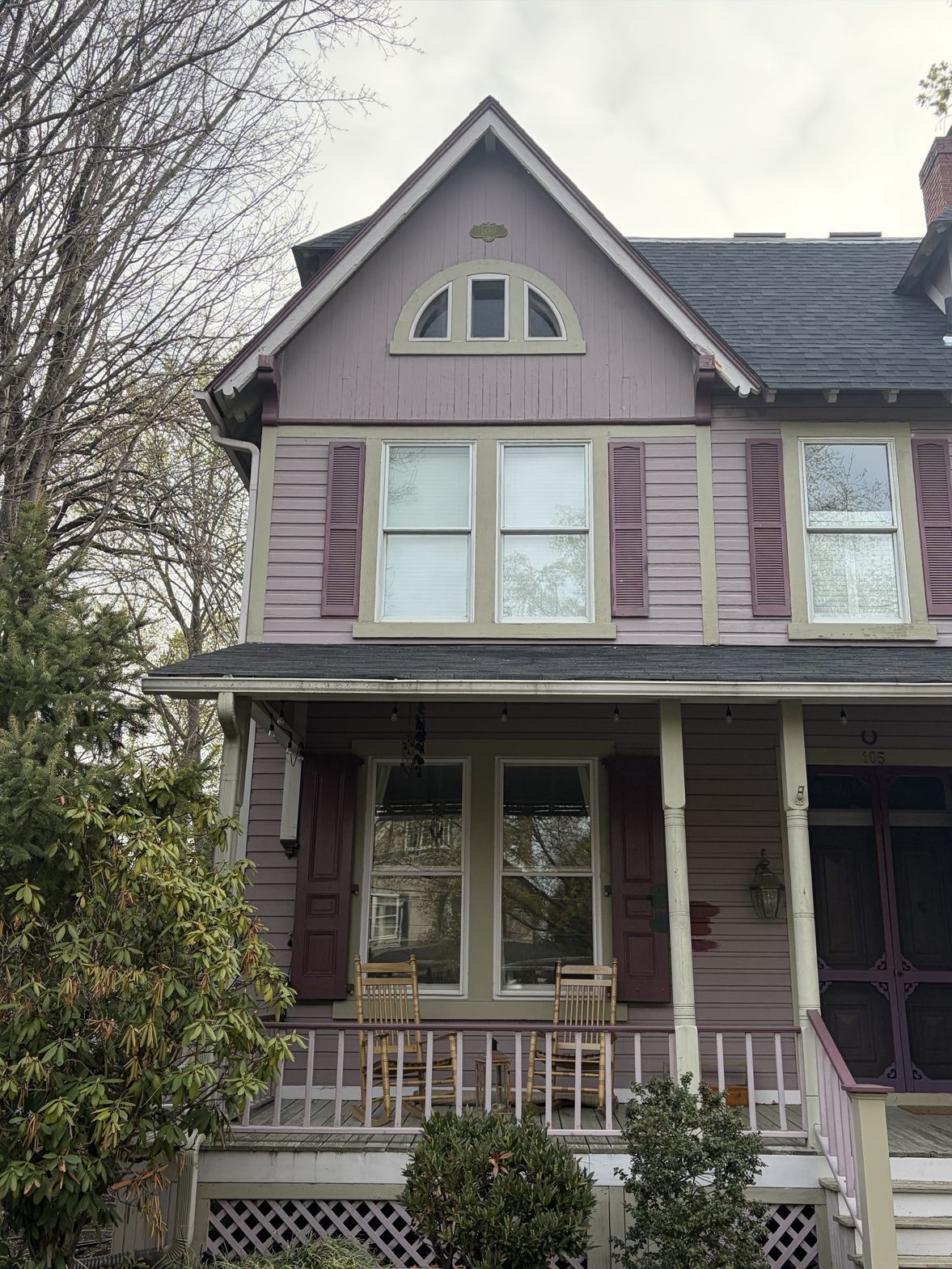 Purple Victorian house with white trim and front porch, partly framed by bare trees