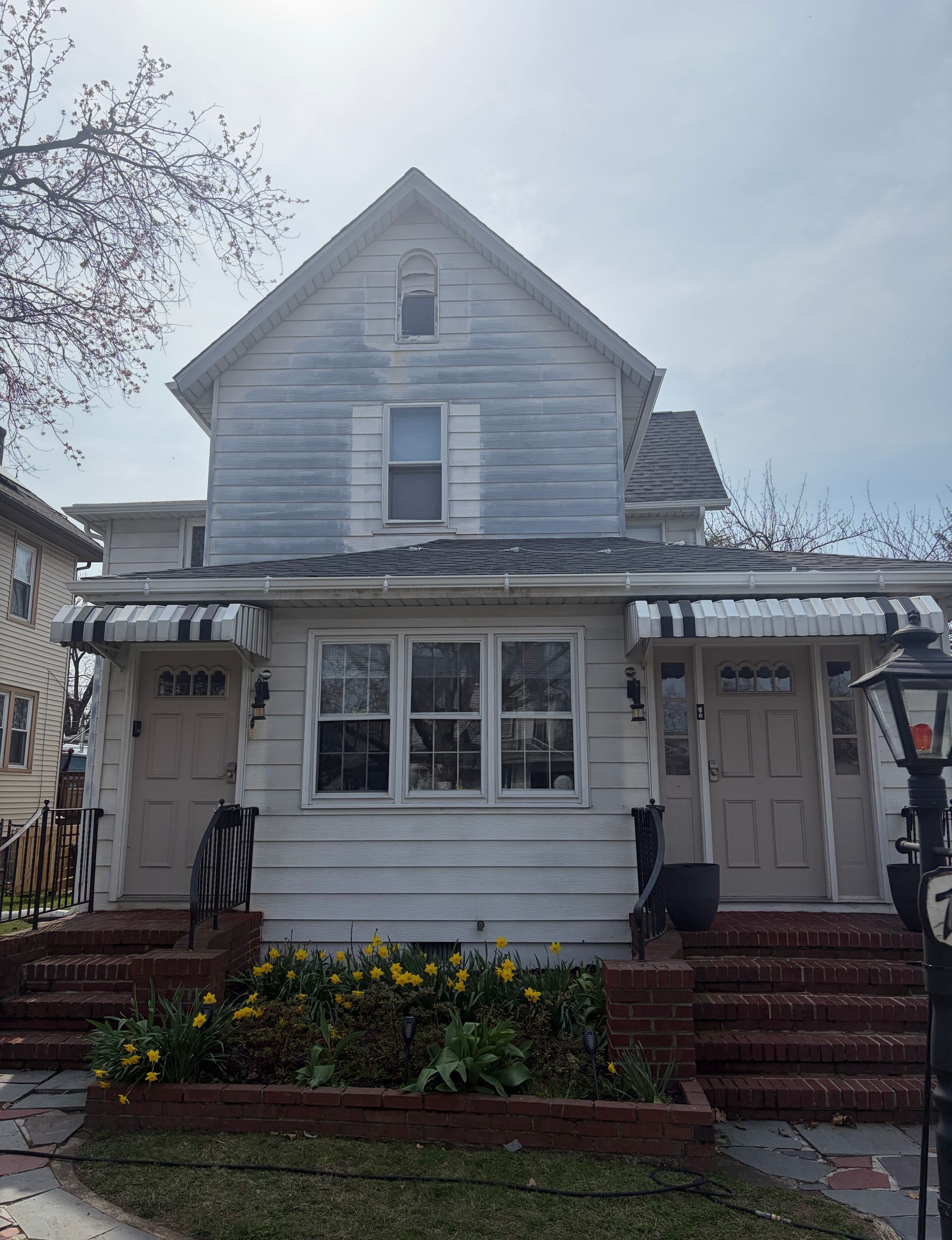 Two-story white house with front porch, red brick steps, and flower bed in front