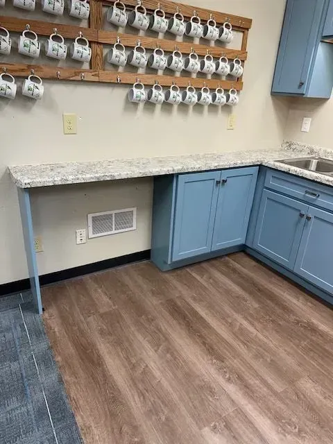 Kitchen with light blue cabinets, speckled countertop, and wooden floor. A rack with mugs is mounted on the wall.