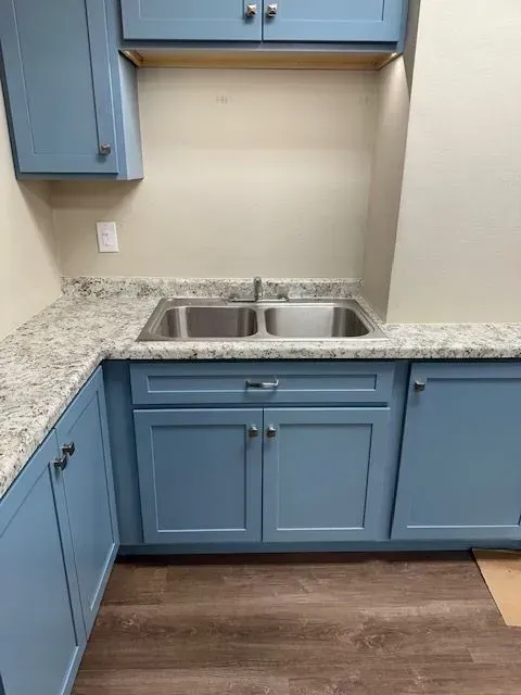Blue kitchen cabinets with a stainless steel double sink and light countertop.
