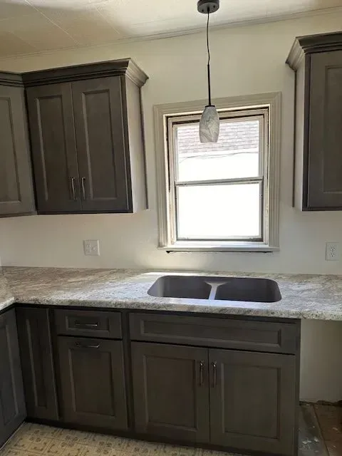 Kitchen with gray cabinets, a window above the sink, and a pendant light.