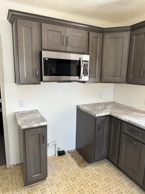 Gray kitchen cabinets with a microwave, corner countertop, and patterned floor.