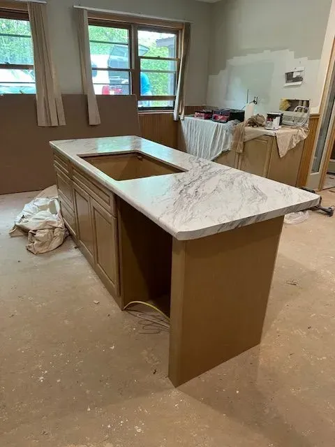 Kitchen island with a marble countertop; cabinets are a light wood color.