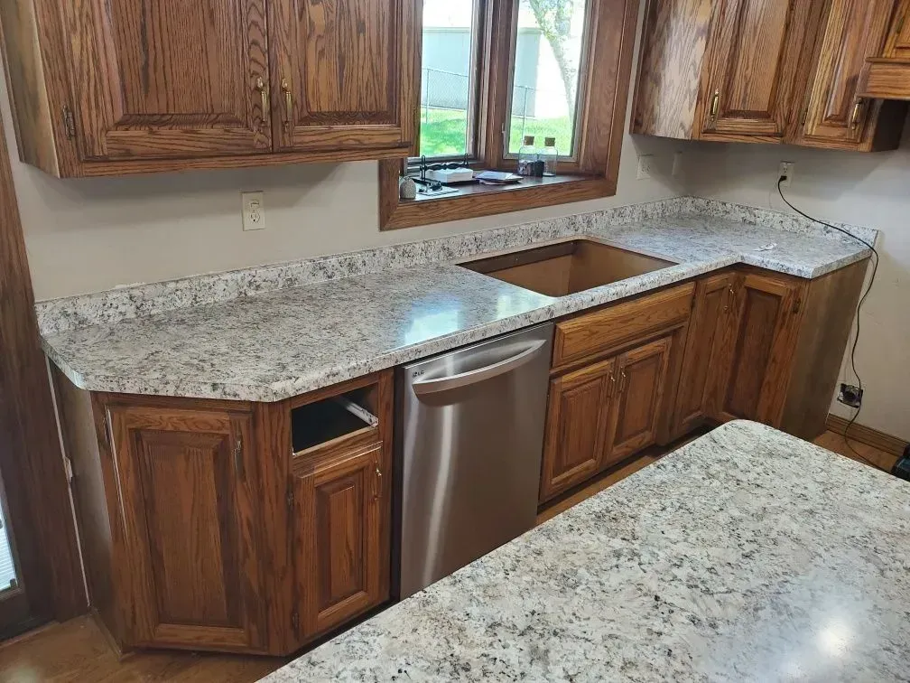 Kitchen with light granite countertops and brown cabinets; dishwasher is installed.