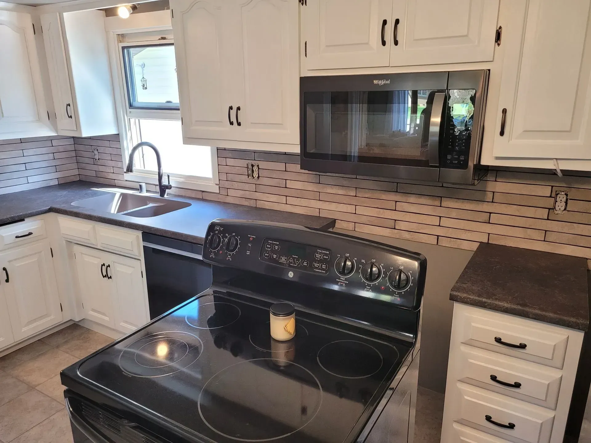 Kitchen with white cabinets, black appliances, and a light brown tile backsplash.