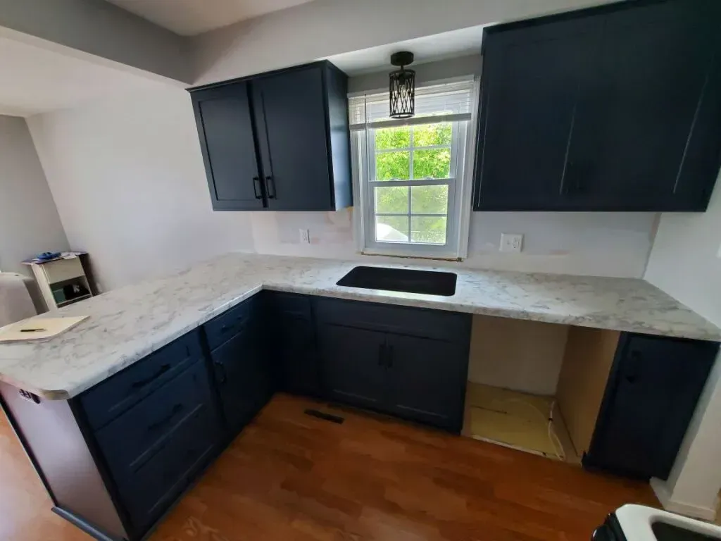 Navy blue kitchen cabinets with white countertops and a window.