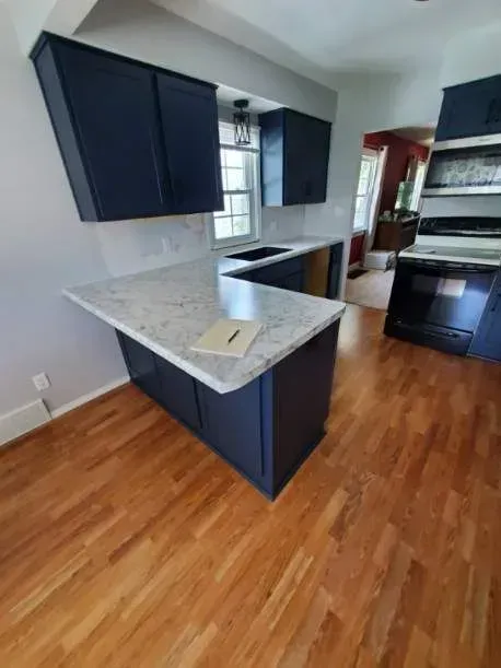 Blue kitchen cabinets and island with white countertop, hardwood floors, and gray walls.