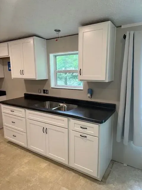 White kitchen cabinets with black countertop, stainless steel sink, and window.