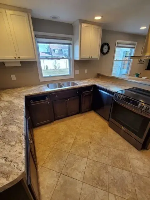 U-shaped kitchen with brown cabinets, cream countertops, light brown tiled floor, and a stainless steel oven.